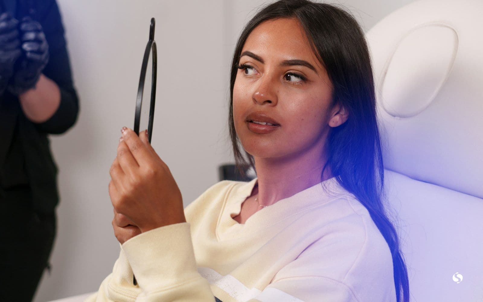 A young woman looking in a hand mirror while she waits